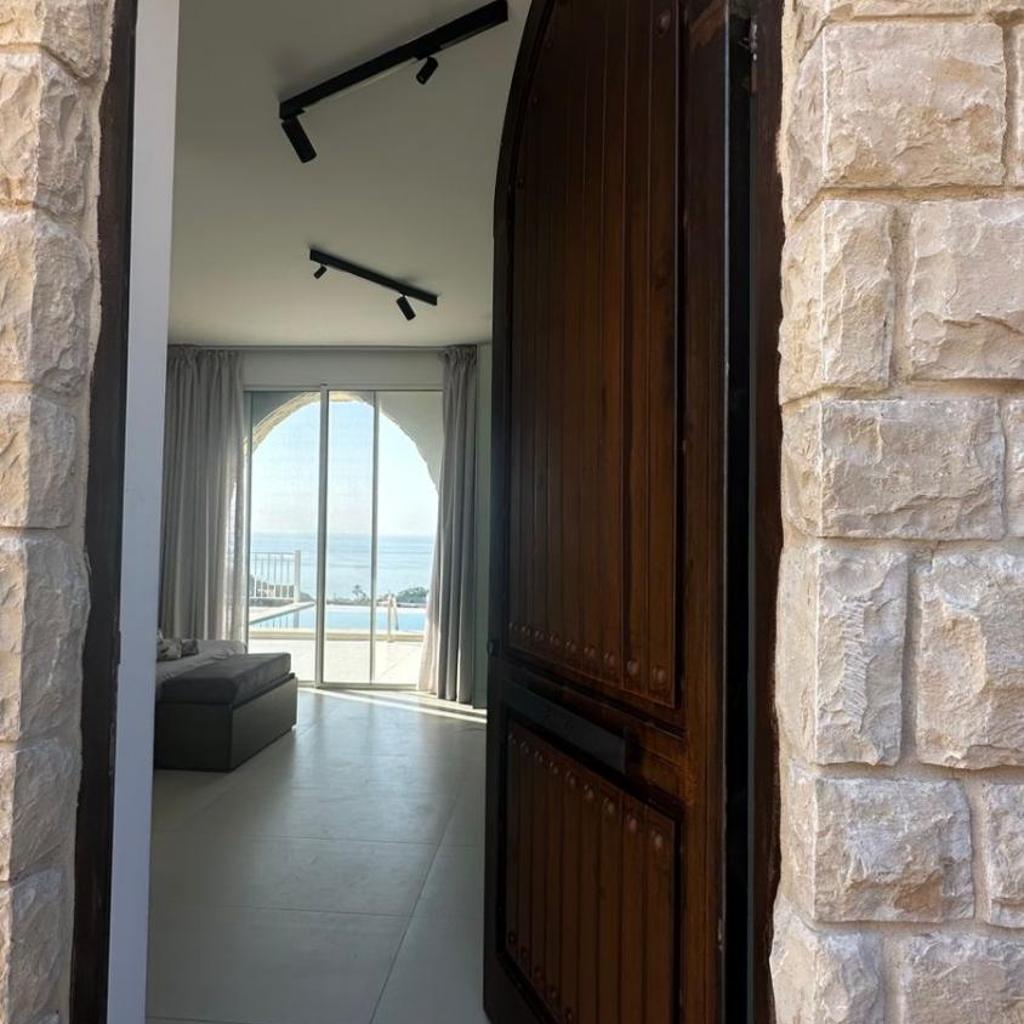 An arched stone doorway leading into a bright room with the sea visible beyond