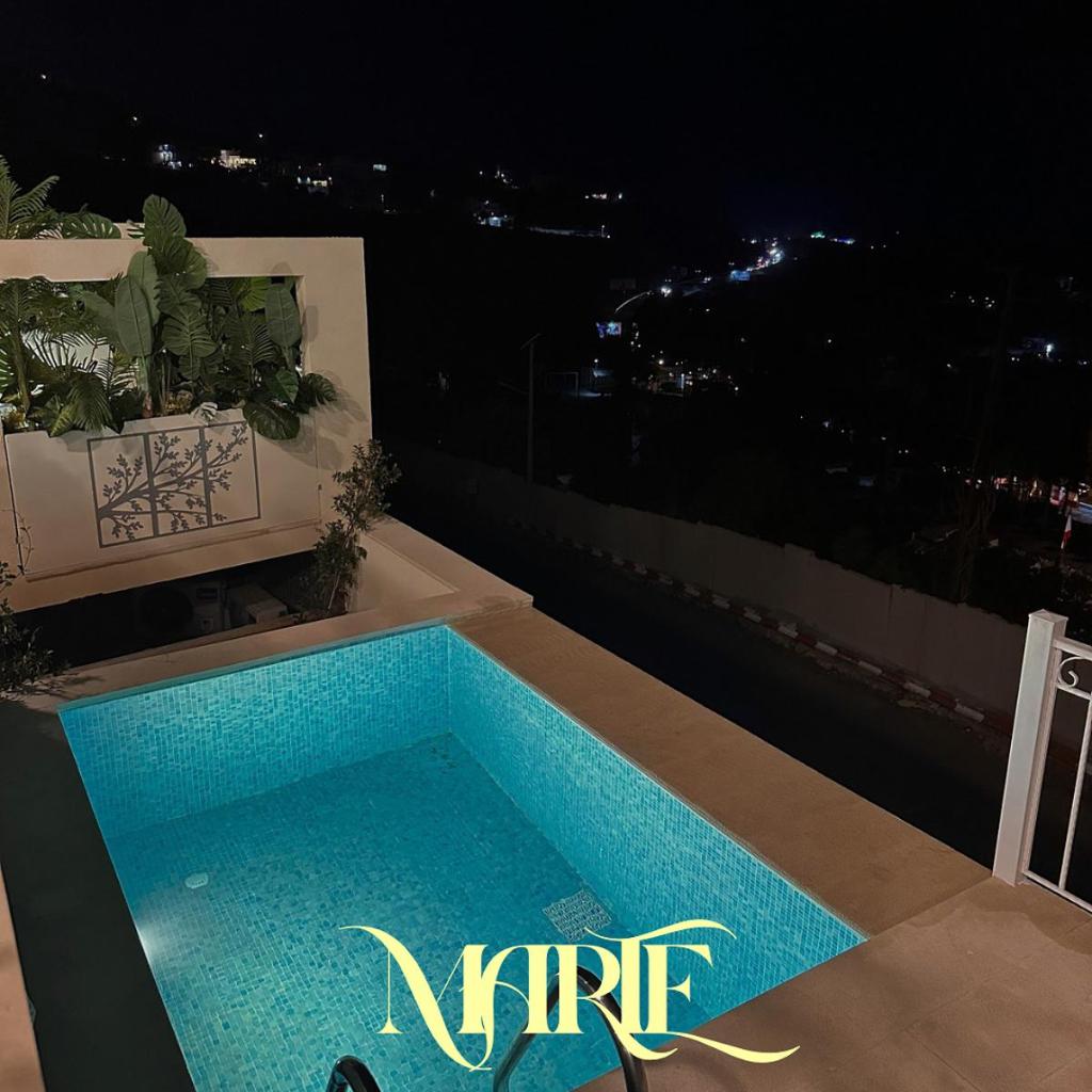 A private pool glowing turquoise at night with the coastal city lights below
